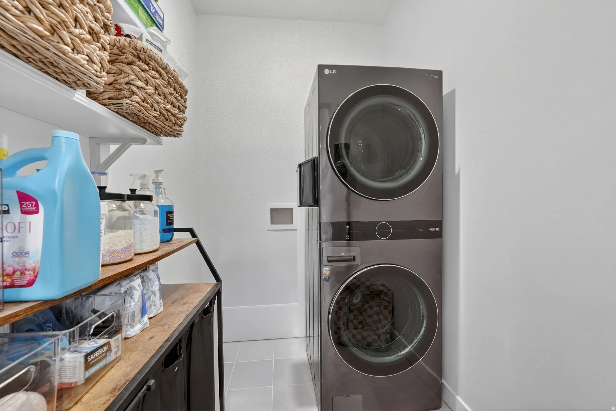 Dedicated laundry area featuring a stacked appliance unit, white wall shelving, and a wood-finish countertop