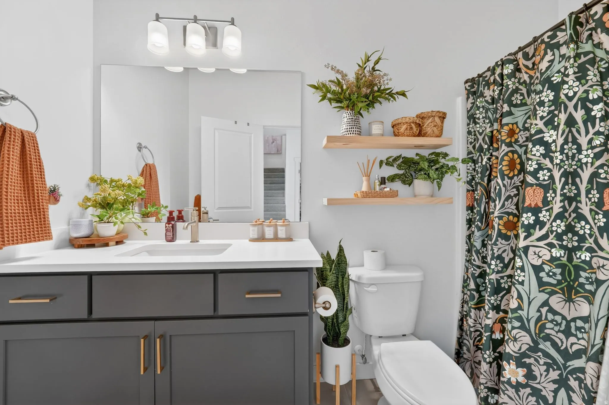 Bathroom featuring a dark gray vanity with gold-tone hardware, white countertop with integrated sink, and an overhead light fixture