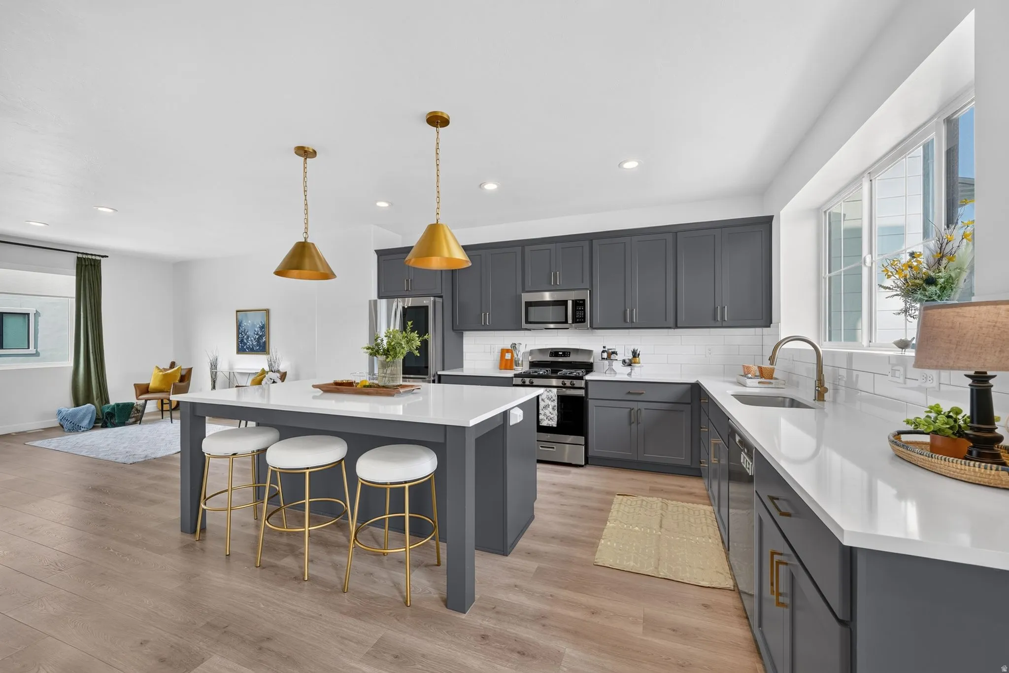 Kitchen featuring a central island with countertop seating, gray cabinetry, stainless steel appliances, white subway tile backsplash, and light wood-finish flooring