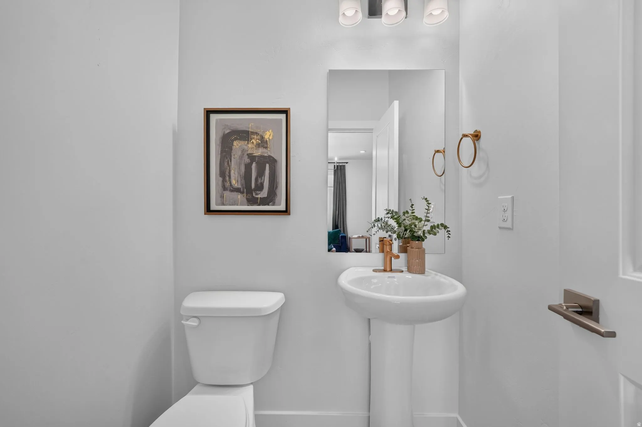 Pedestal sink with a bronze-finish faucet, mirror, and overhead vanity lighting