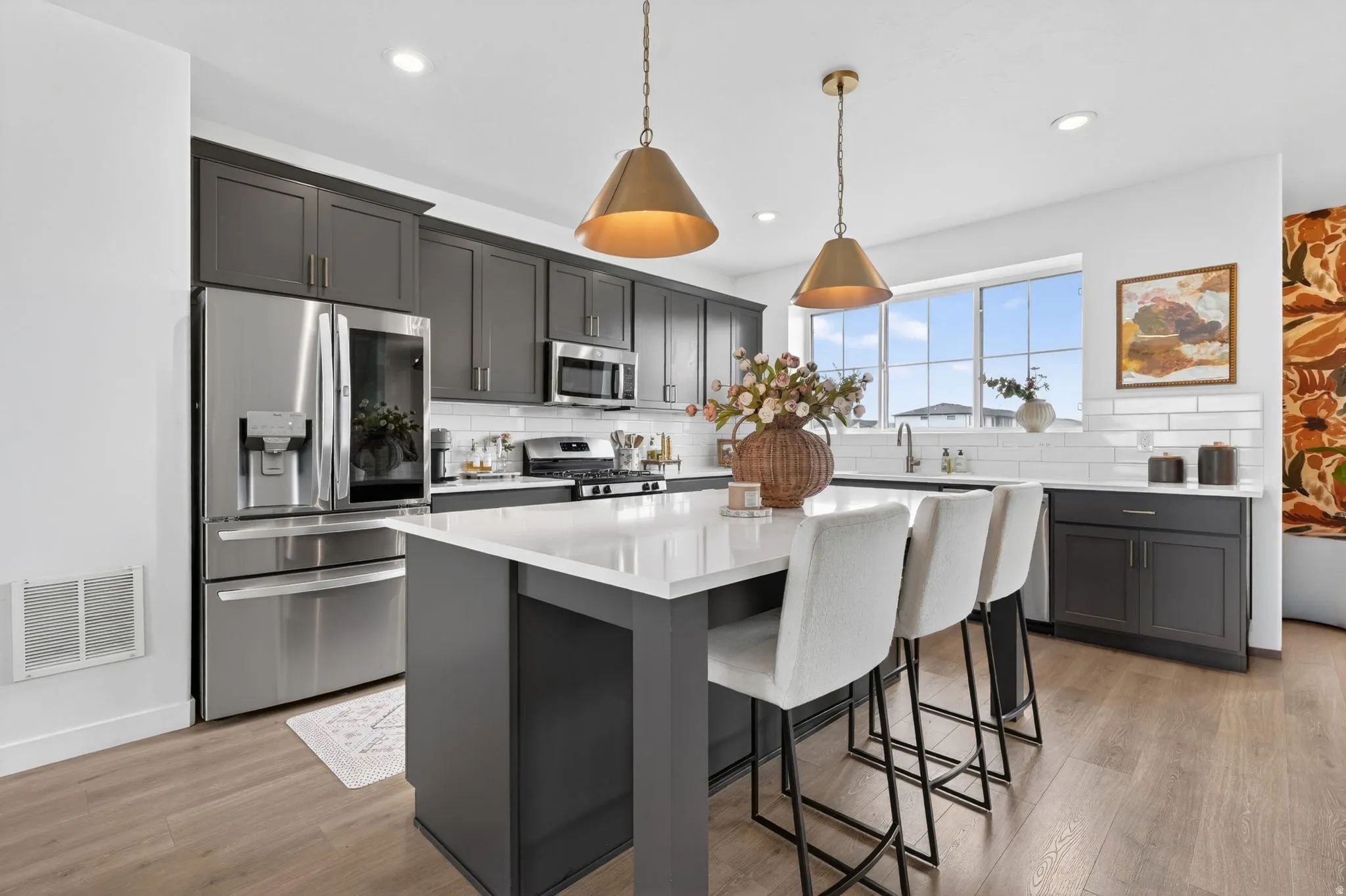 Contemporary kitchen featuring dark cabinetry, stainless steel appliances, a center island with seating, and wood-finish flooring