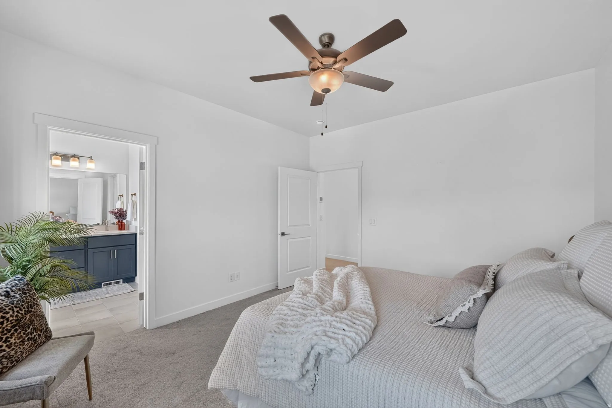 Carpeted bedroom featuring a ceiling fan with light fixture and a privacy door leading to a bathroom