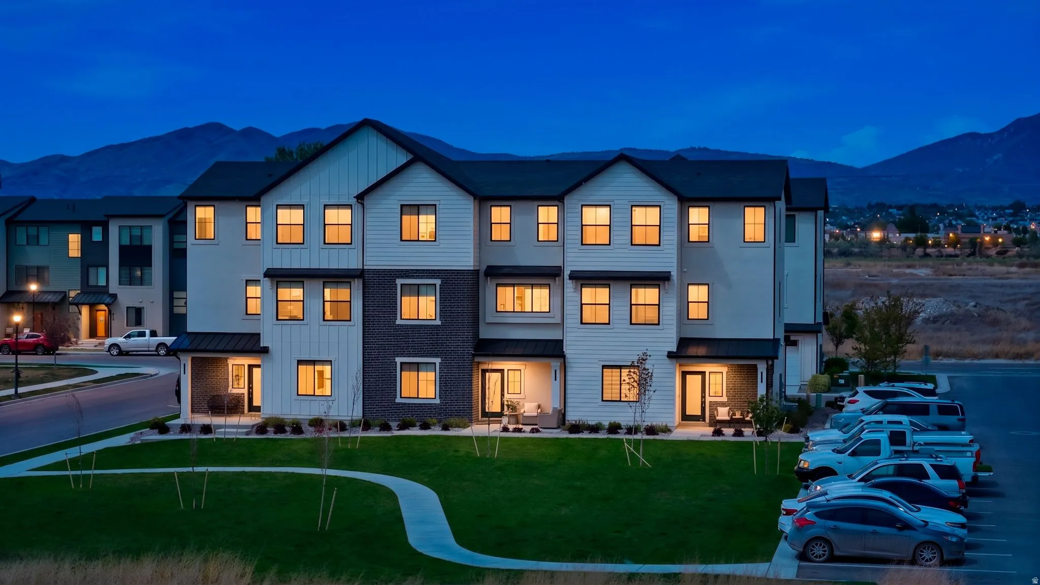 Modern multi-story residential building featuring a dark shingle roof, white vertical siding, and dark brick accents