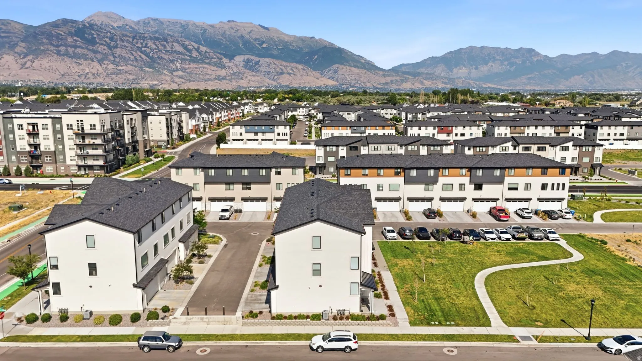Contemporary townhome community featuring a mountain backdrop, integrated garages, manicured green space, and pedestrian pathways