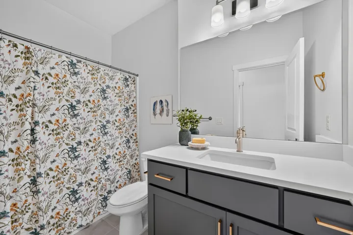 Bathroom featuring a dark gray vanity with gold-tone hardware, a white countertop with an integrated sink, and a large mirror