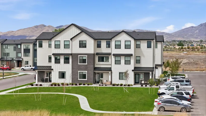 Modern townhome exterior featuring white vertical and horizontal siding, dark brick accents, black-framed windows, and a covered entry