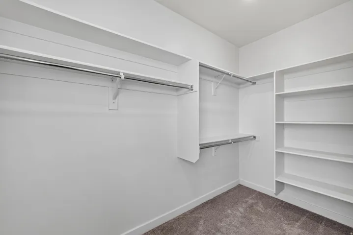 Walk-in closet featuring built-in shelving, multiple hanging rods, and a neutral carpeted floor