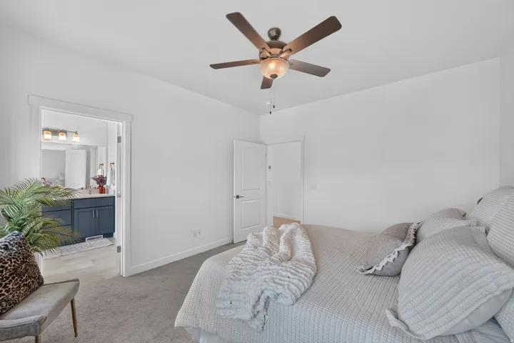Carpeted bedroom featuring a ceiling fan with light fixture and a privacy door leading to a bathroom
