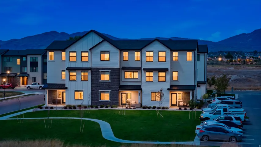 Modern multi-story residential building featuring a dark shingle roof, white vertical siding, and dark brick accents