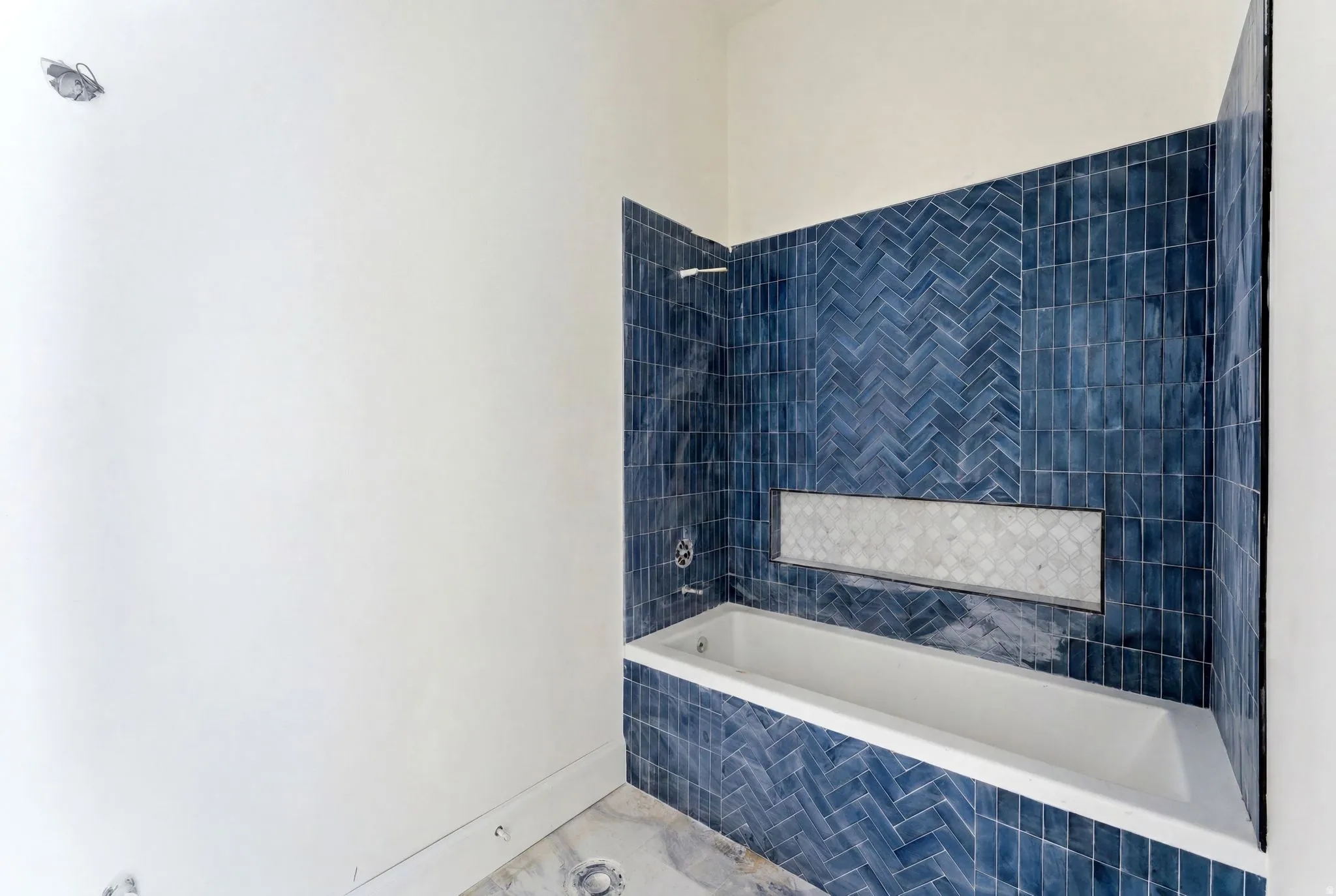 White bathtub with a built-in niche featuring a mosaic tile inlay