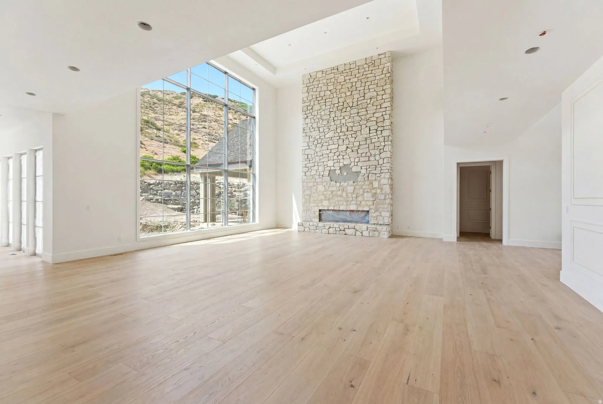 Expansive room featuring a floor-to-ceiling stone fireplace with a linear insert, wide plank wood-finish flooring, and a dramatic two-story window