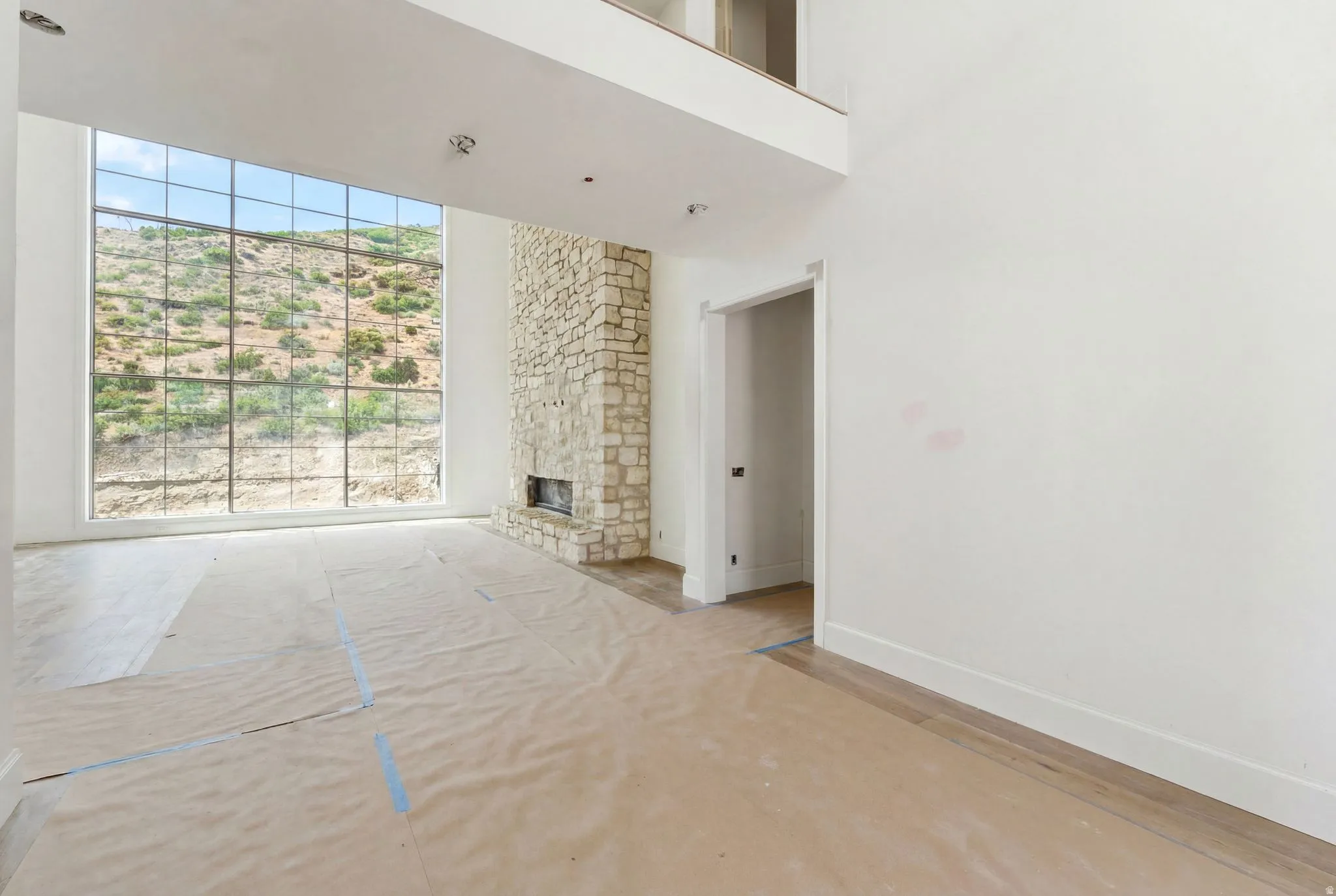 Great room featuring a full-height stone fireplace, expansive window with grid pattern, high ceilings, and wood-finish flooring