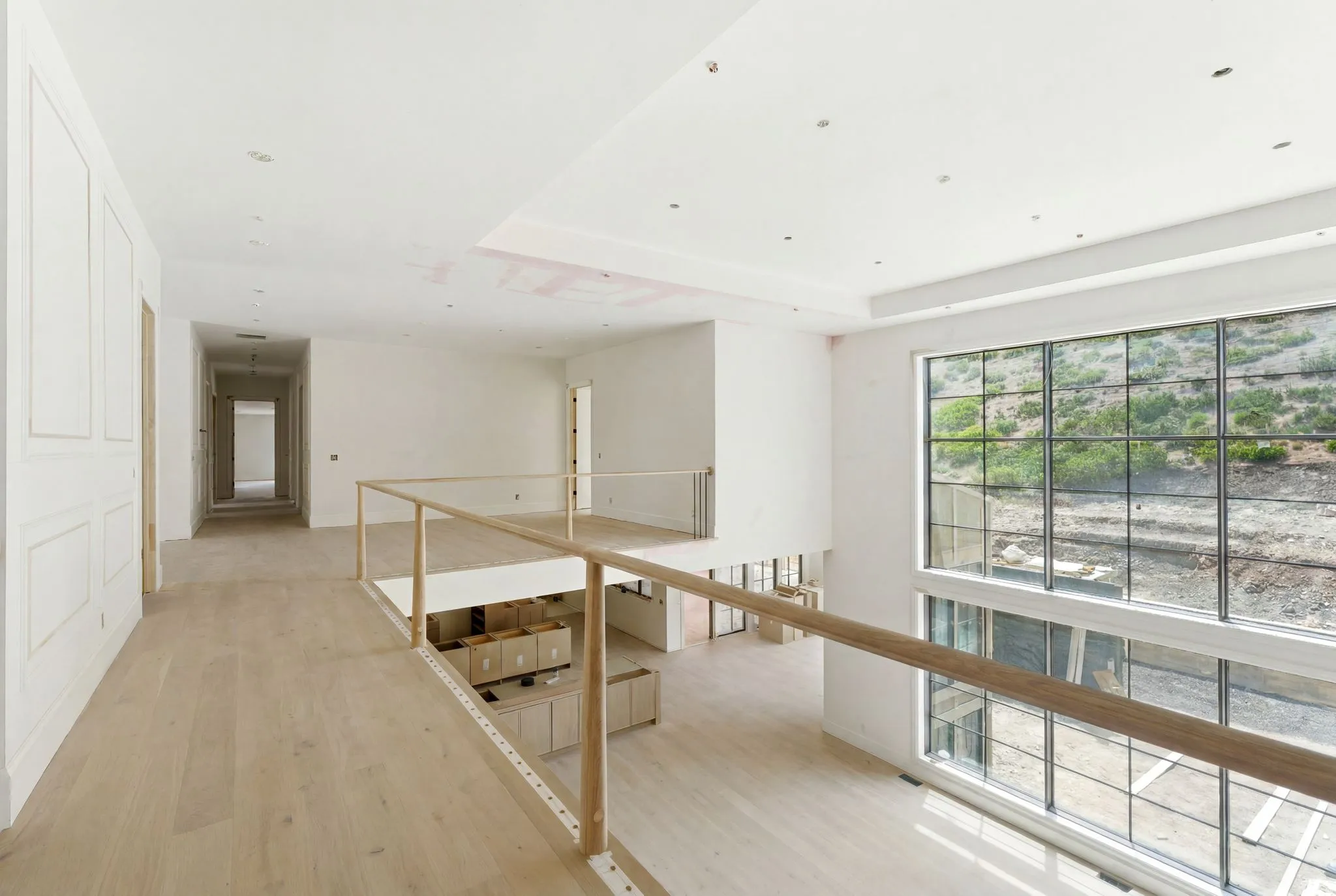 Spacious upper-level landing with light wood-finish flooring, recessed lighting, and a large multi-pane picture window