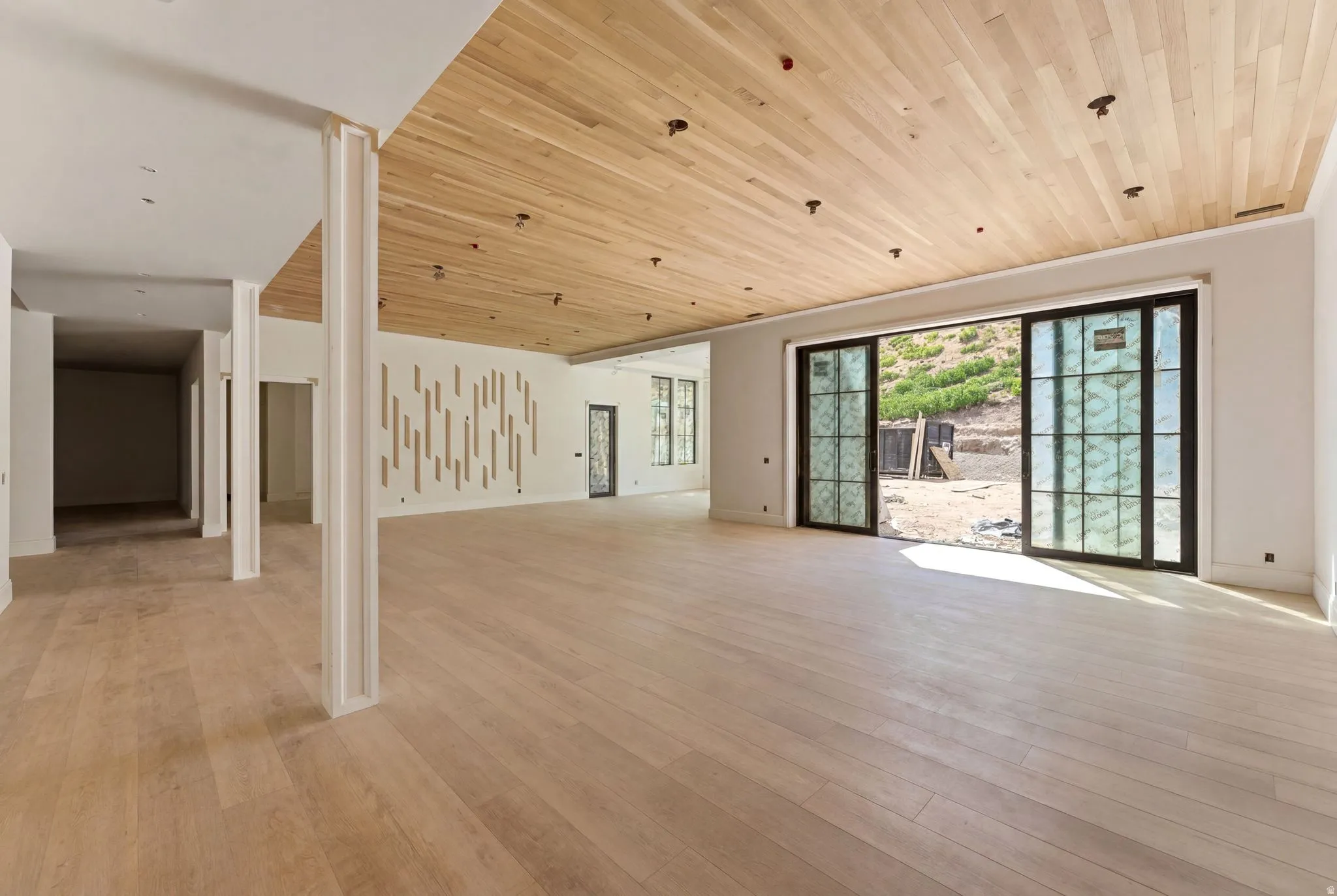 Expansive interior space featuring light wood-finish flooring, a coordinating wood-paneled ceiling with recessed lighting, and a prominent decorative wall paneling