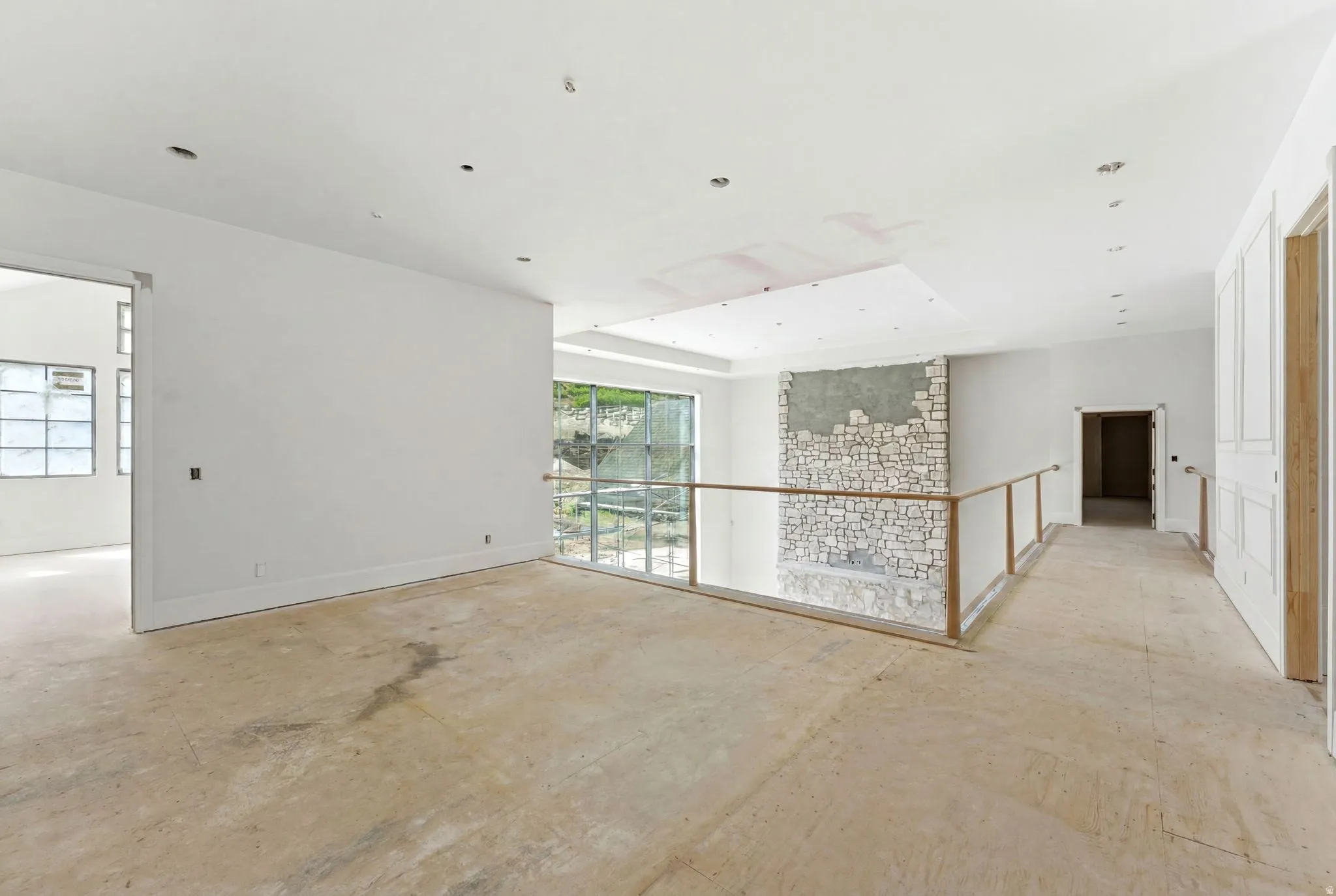 Open concept upper level featuring a stone-clad architectural feature, glass panel railing, recessed lighting, and large windows