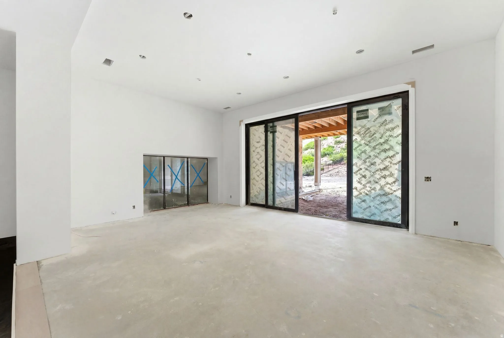 Spacious unfinished interior featuring a large sliding glass door, recessed lighting, and a built-in alcove with glass doors