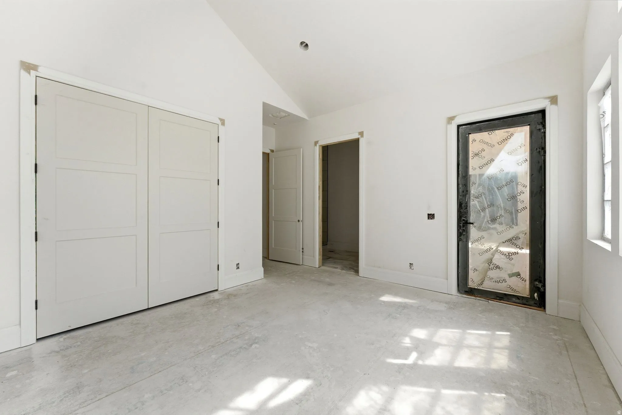 Spacious room featuring vaulted ceilings, a large paneled bi-fold door, a black-framed door with a glass insert, and window openings