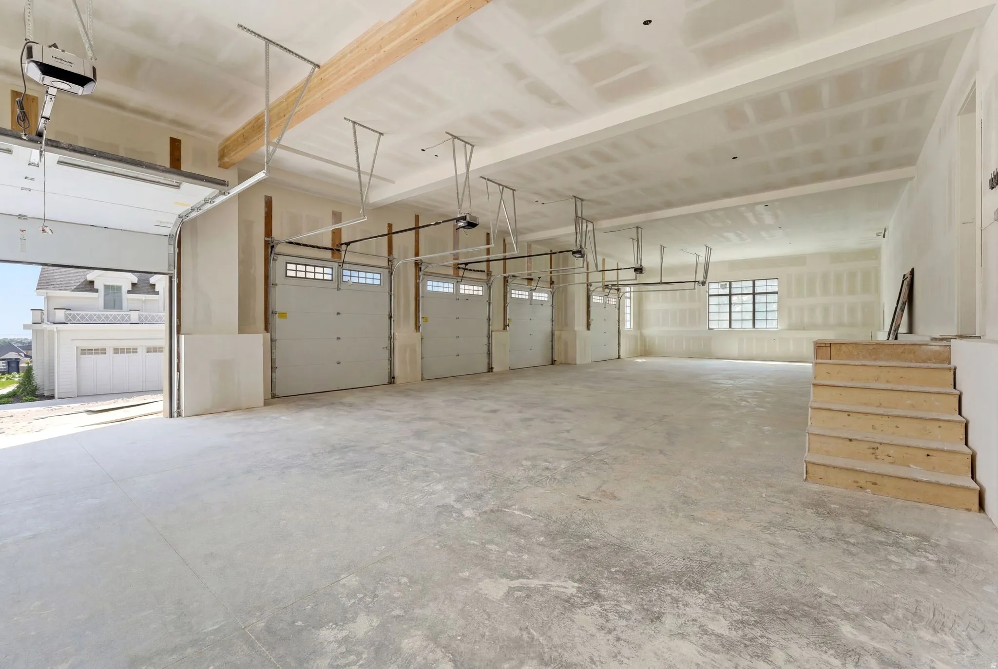 Spacious garage featuring a concrete floor, four overhead doors, exposed wood beams, and multiple windows providing natural light