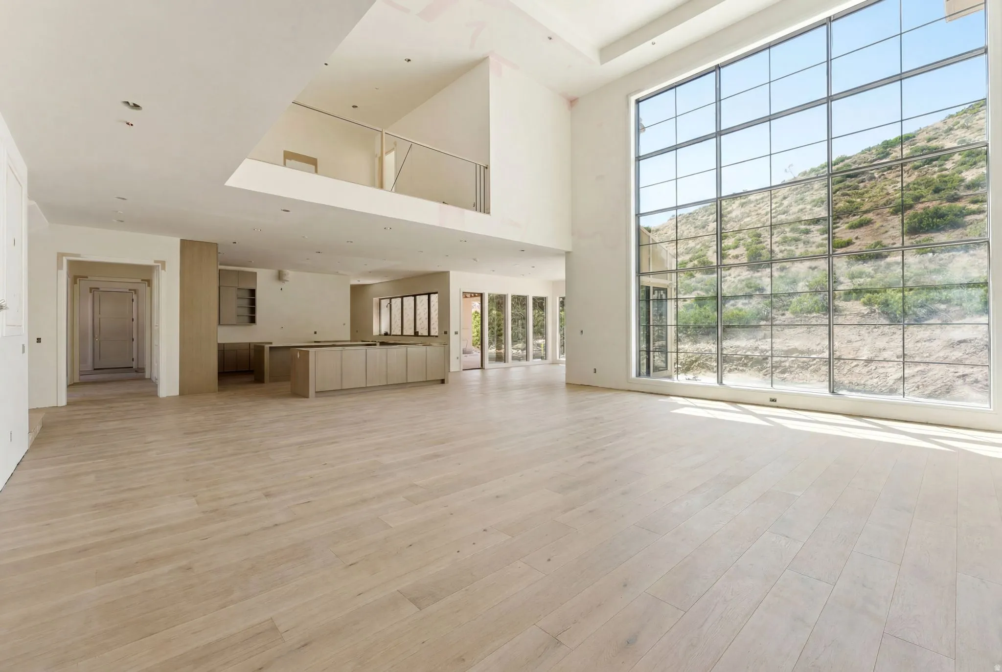 Expansive living area featuring a two-story window wall, wood-finish flooring, and a second-story overlook with a metal railing