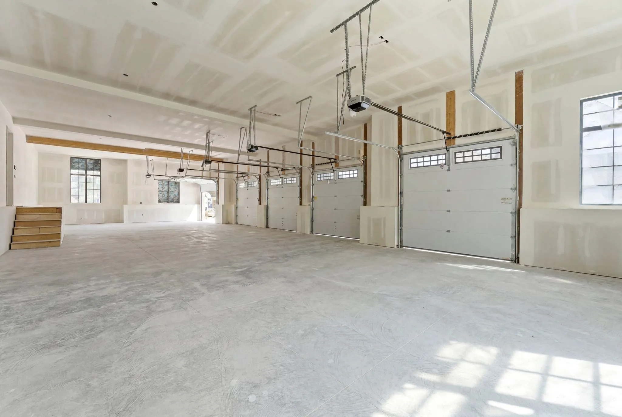 Spacious garage structure featuring multiple overhead doors with transom windows, exposed wood support beams, and a concrete floor