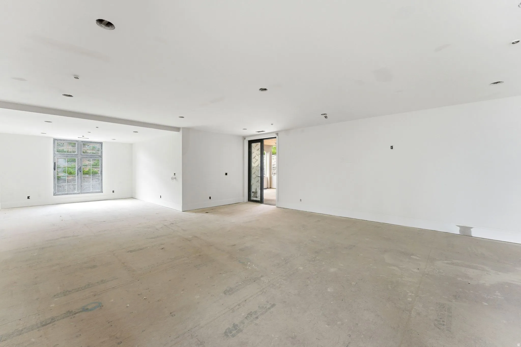Spacious interior room featuring white walls, recessed ceiling lighting, a large multi-pane window, and an exterior glass door