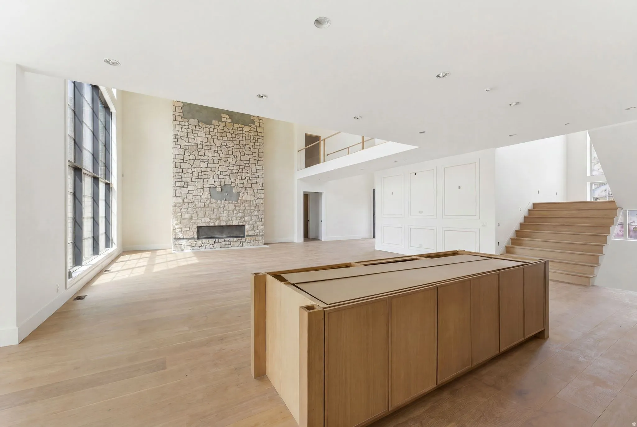 Expansive interior space featuring a floor-to-ceiling stone fireplace, large multipane windows, and wood-finish flooring