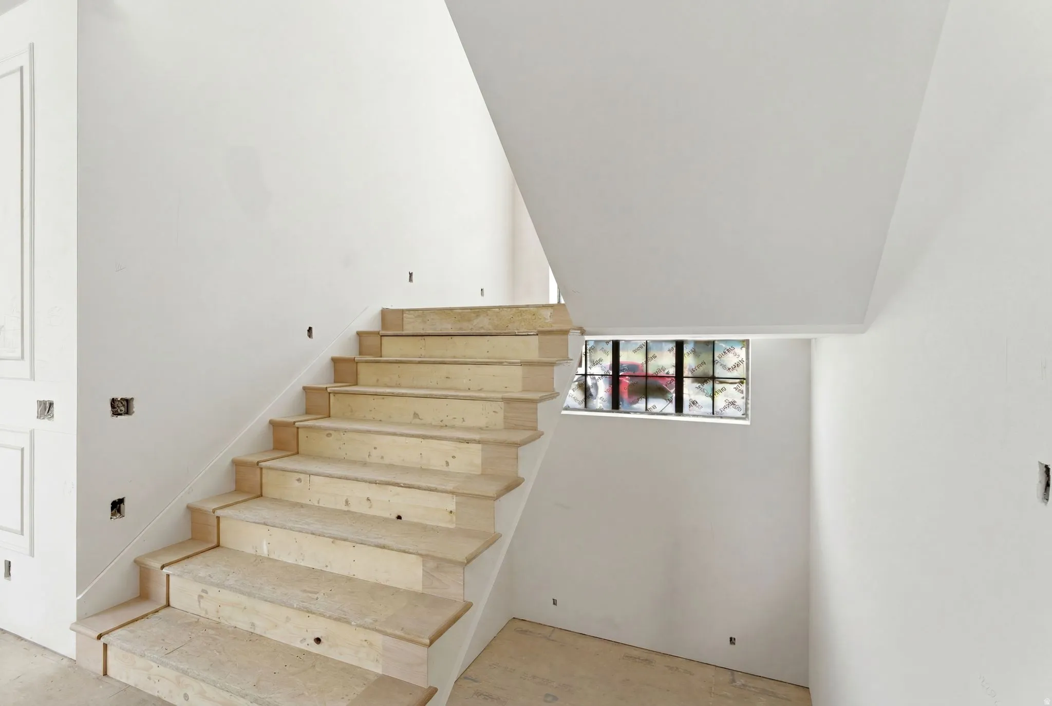 Unfinished wooden staircase with a glass block window and white walls