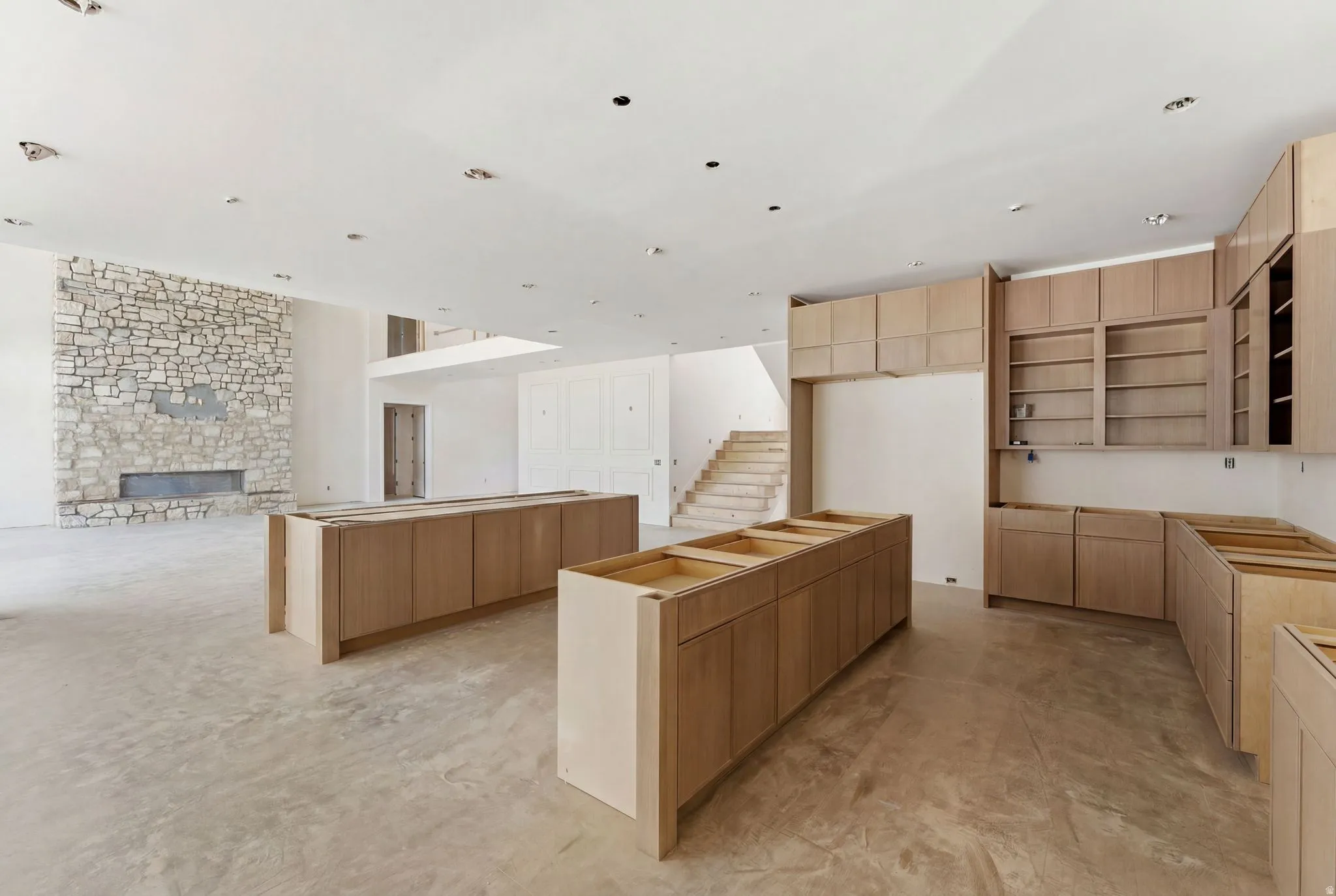 Expansive interior space featuring a stone fireplace, recessed lighting, and light wood cabinetry