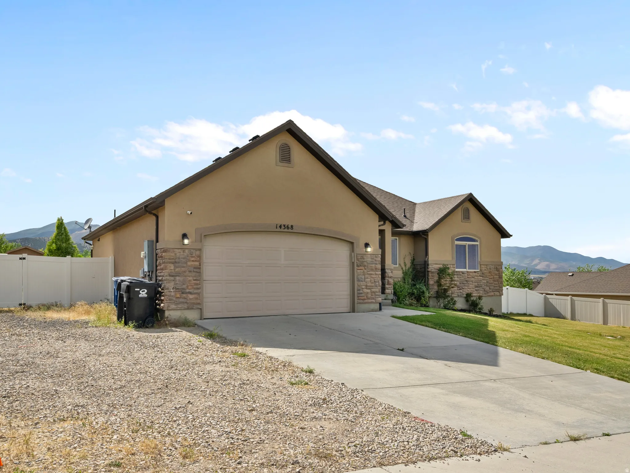 Stucco and stone exterior featuring an arched garage door, concrete driveway, and a partially manicured lawn