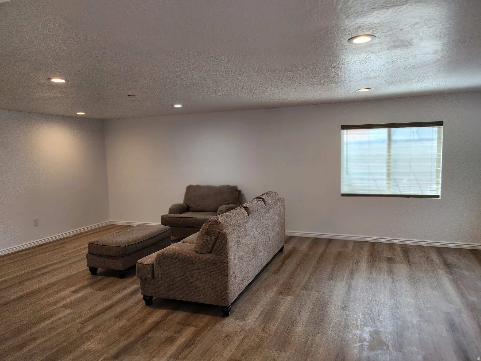 Spacious room featuring wood-finish flooring, recessed lighting, and a window with blinds