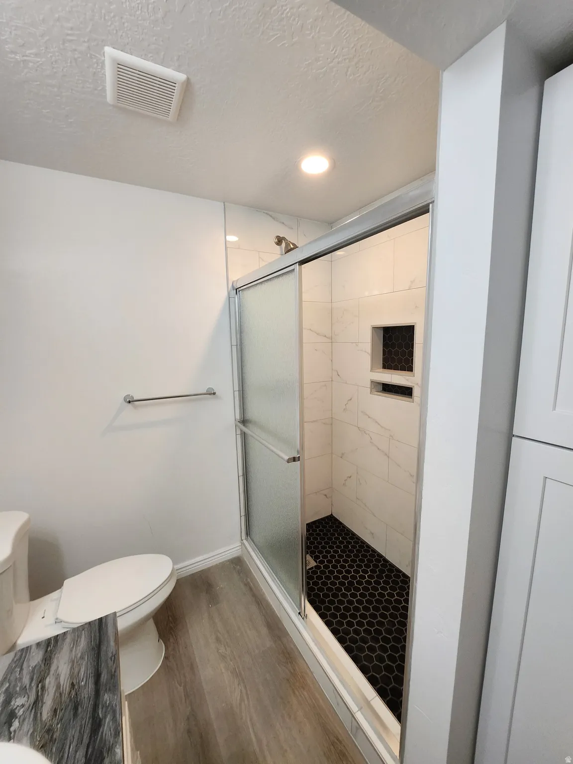 Modern shower with white marble-patterned tile, black hexagonal floor tiles, and a recessed niche