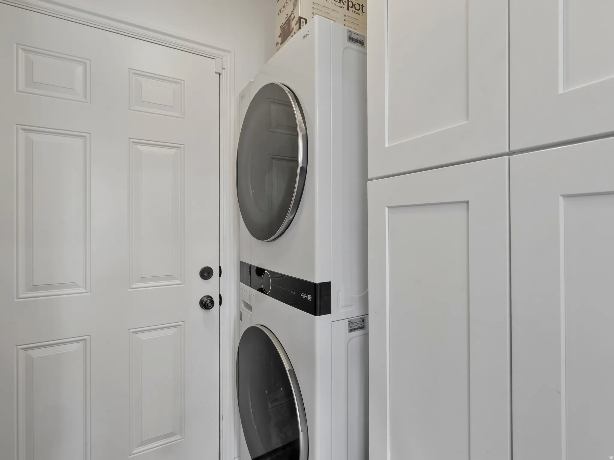 Dedicated laundry area featuring a stacked washer and dryer, shaker-style cabinetry, and a paneled door