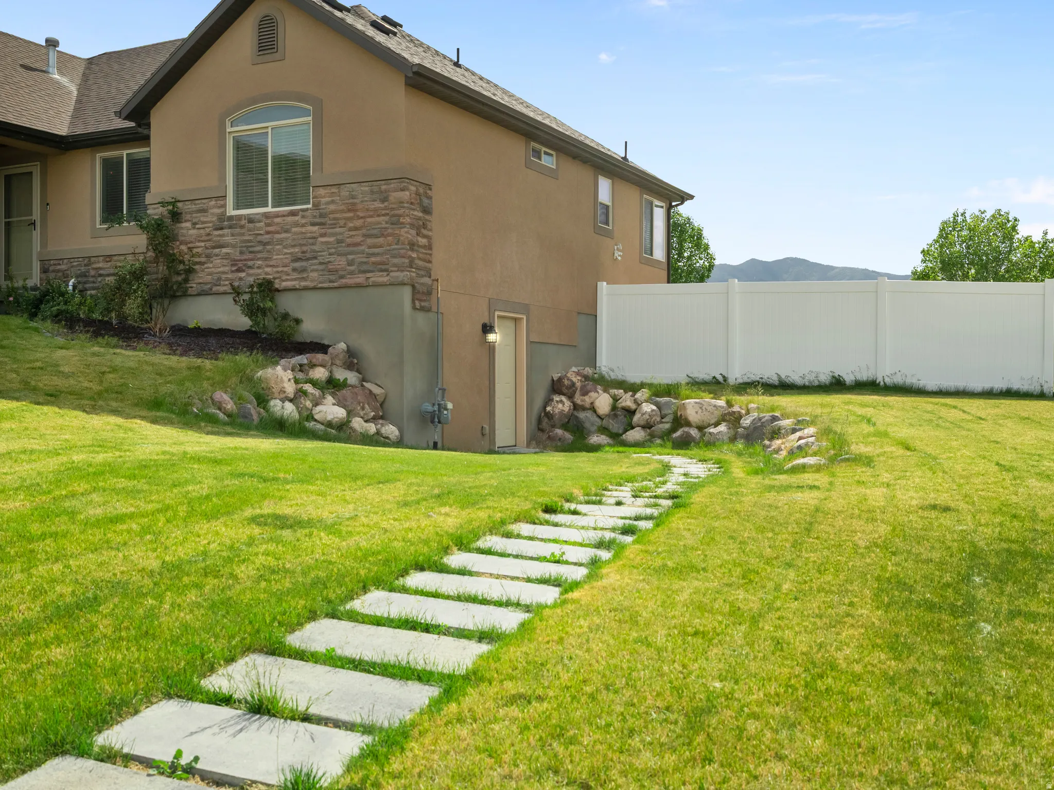 Expansive green lawn with a stepping stone pathway, complemented by a white privacy fence
