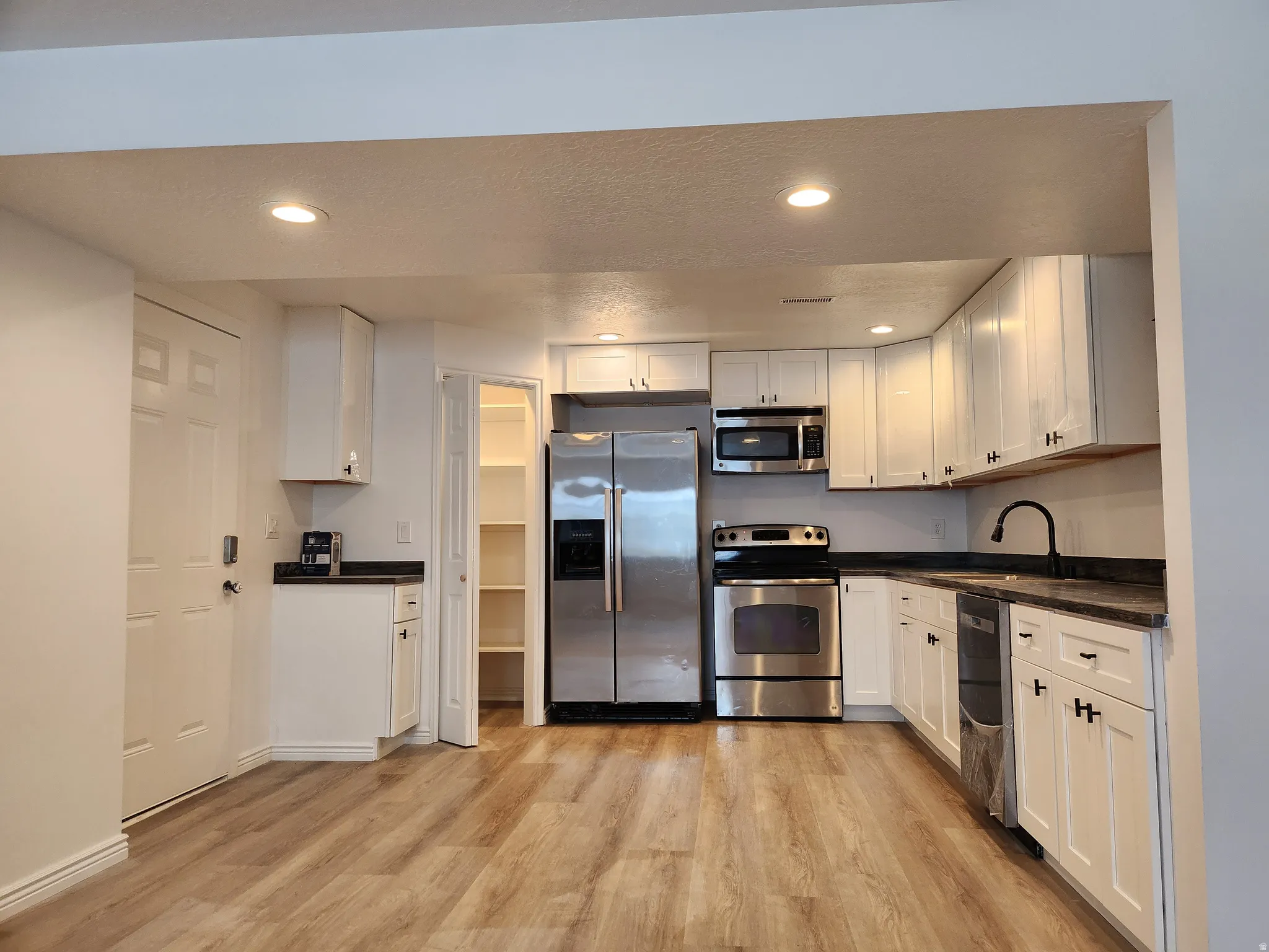 Kitchen featuring stainless steel appliances, white cabinetry with dark hardware, dark countertops, and wood-finish flooring