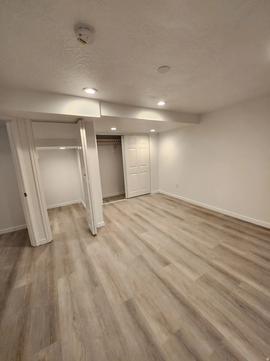 Spacious room featuring wood-finish flooring, recessed lighting, and multiple closet spaces