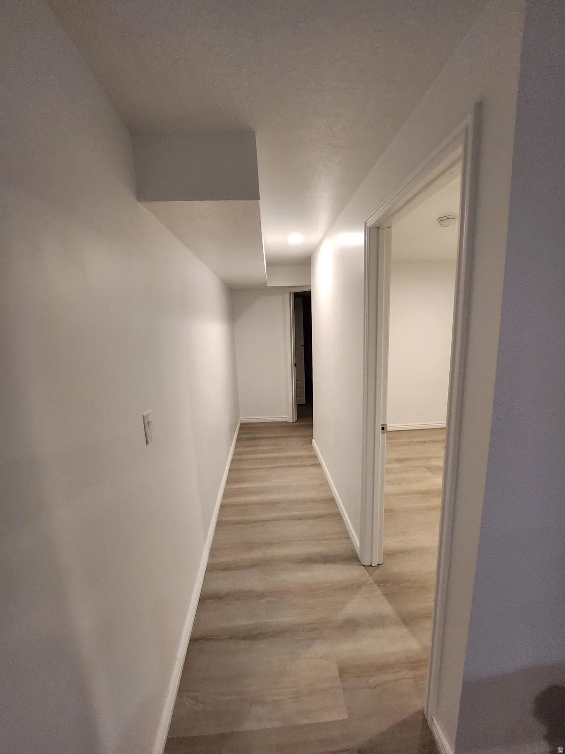 Hallway with wood-finish flooring, white baseboards, and bright white walls