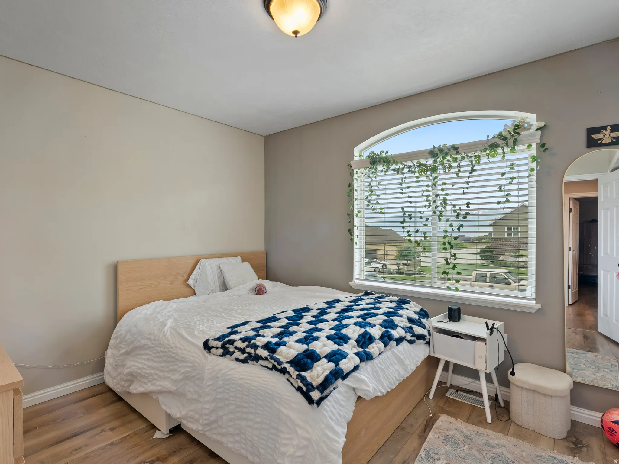 Room featuring an arched window with blinds, wood-finish flooring, and neutral wall tones