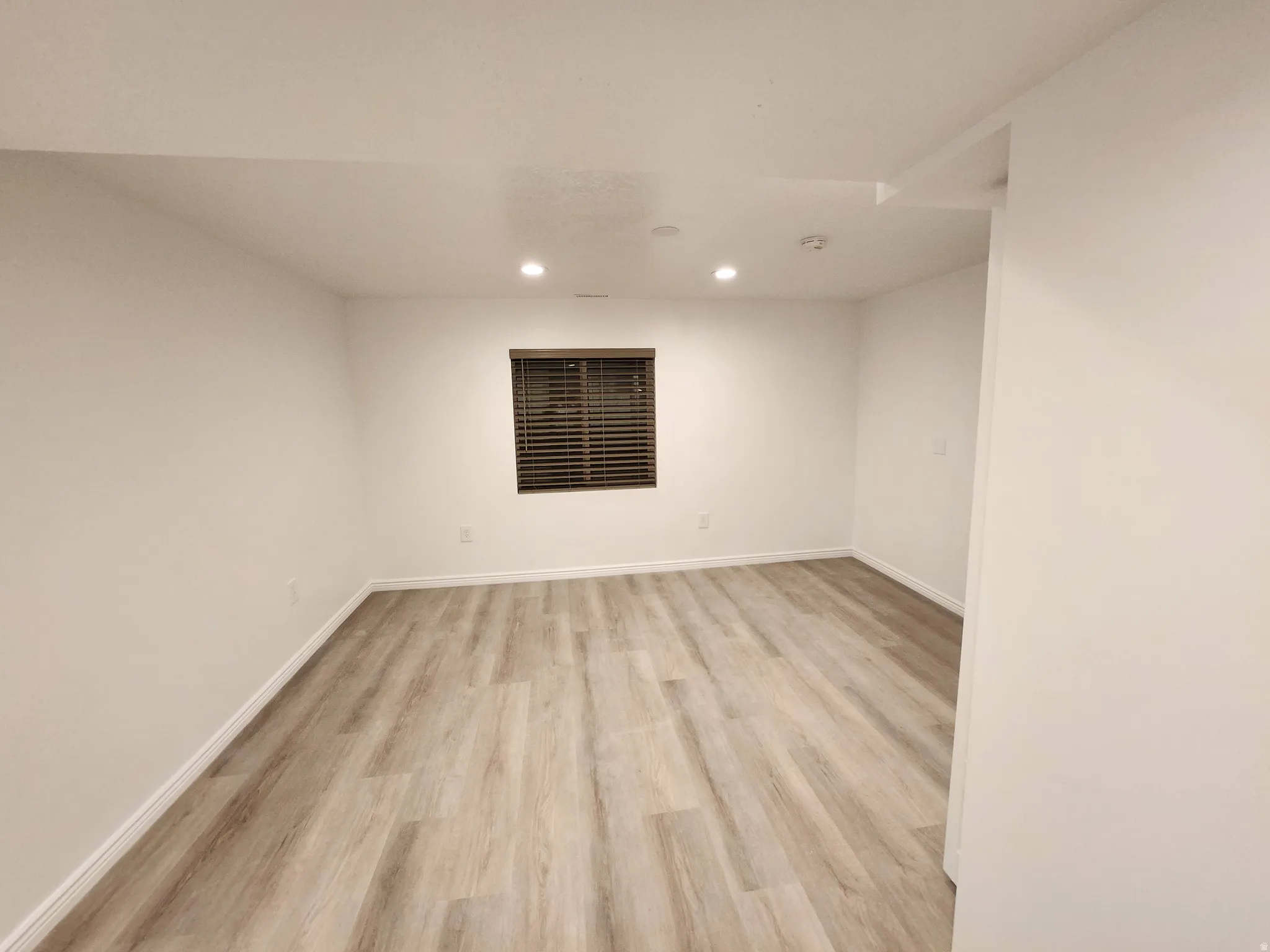 Spacious room featuring light-toned wood-finish flooring, white walls, and recessed lighting