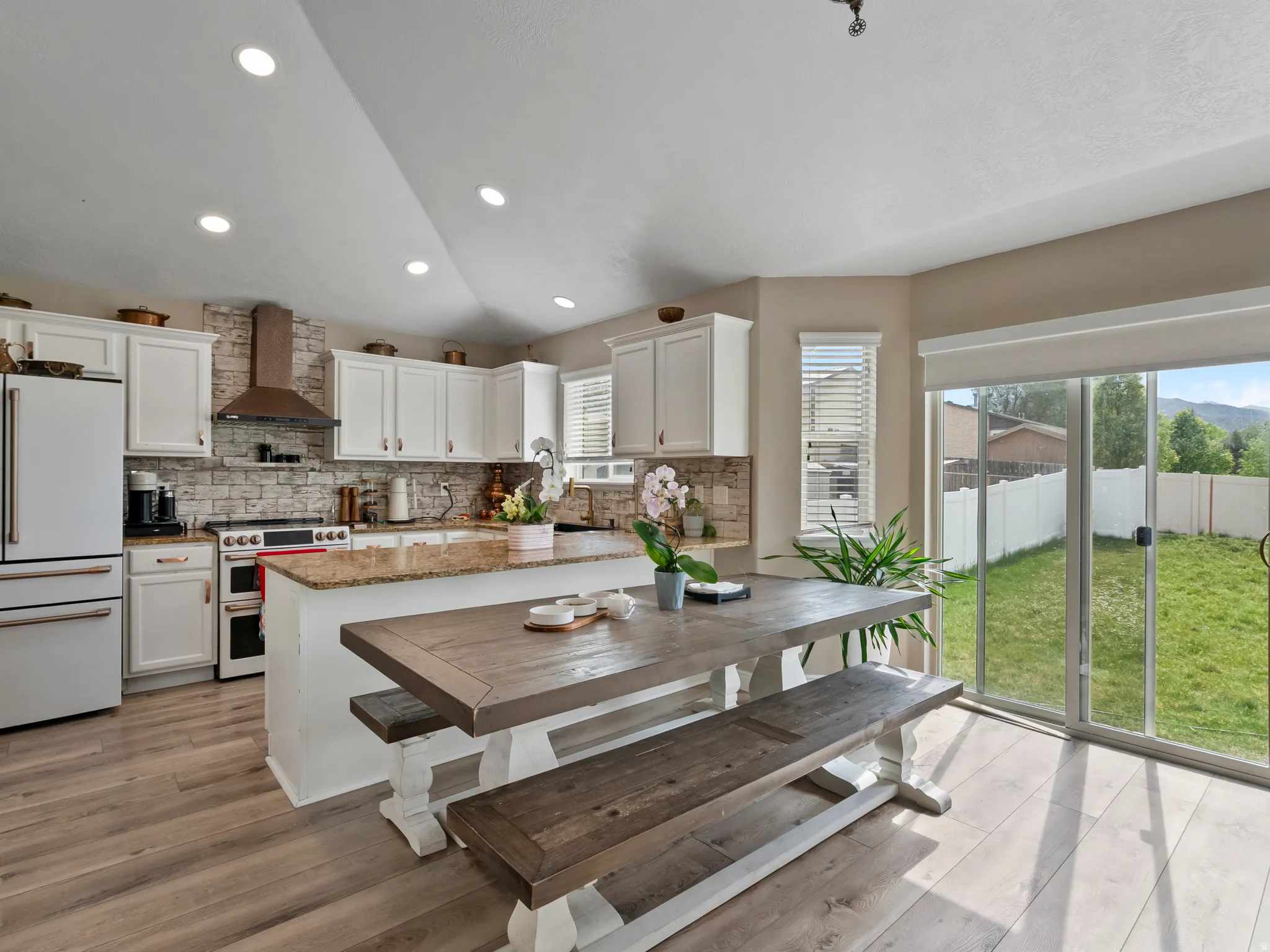 Open-concept kitchen featuring white cabinetry, a stone-look backsplash, stainless steel appliances, and a central island with a granite-look countertop