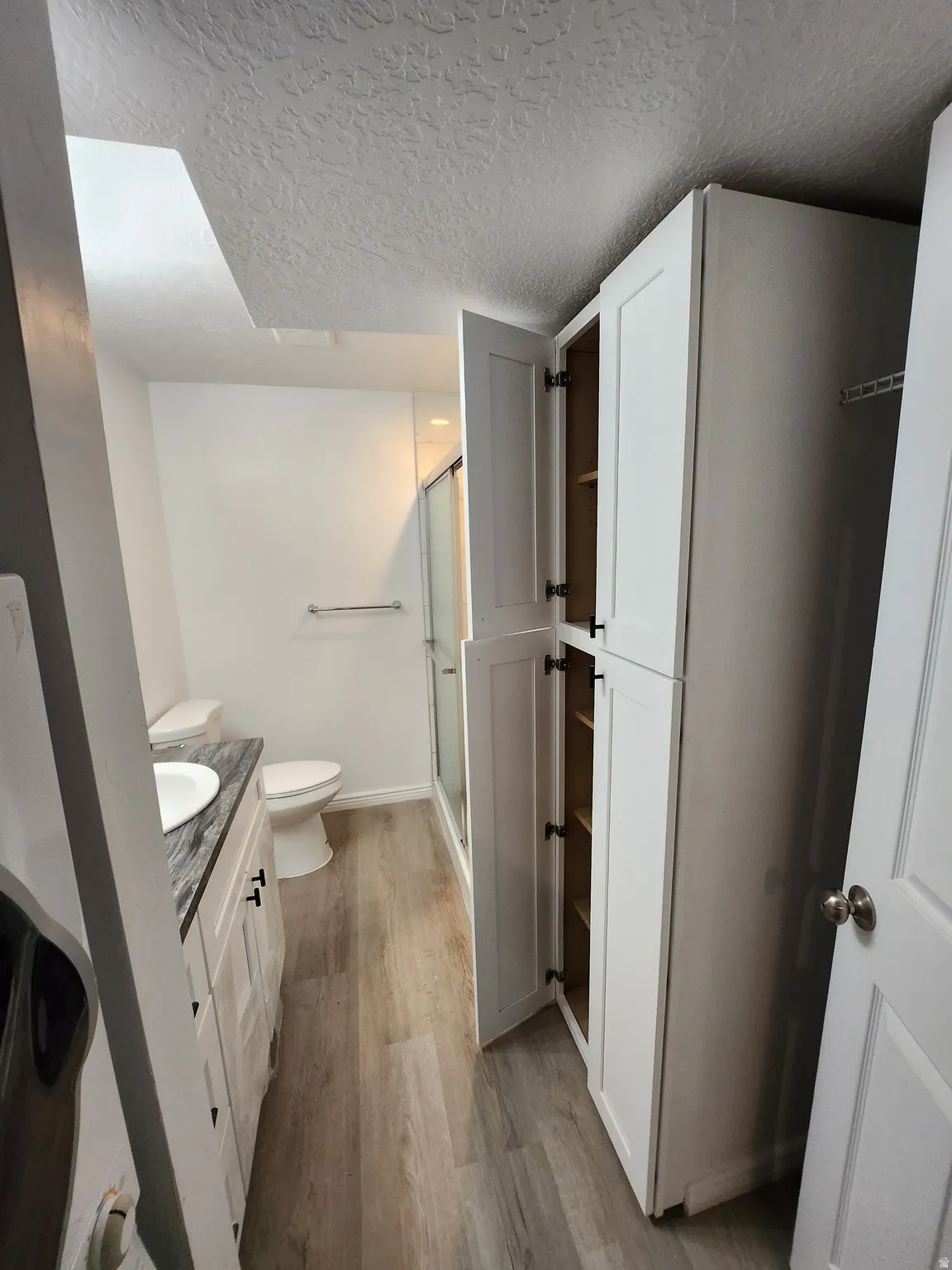 Bathroom featuring light wood-finish flooring, a white vanity with dark countertop, a white toilet, and a glass-enclosed shower