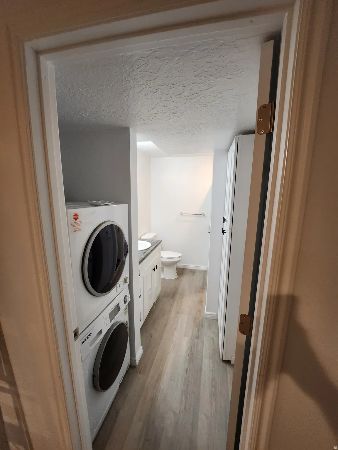 Dedicated laundry area featuring stacked appliances and wood-finish flooring