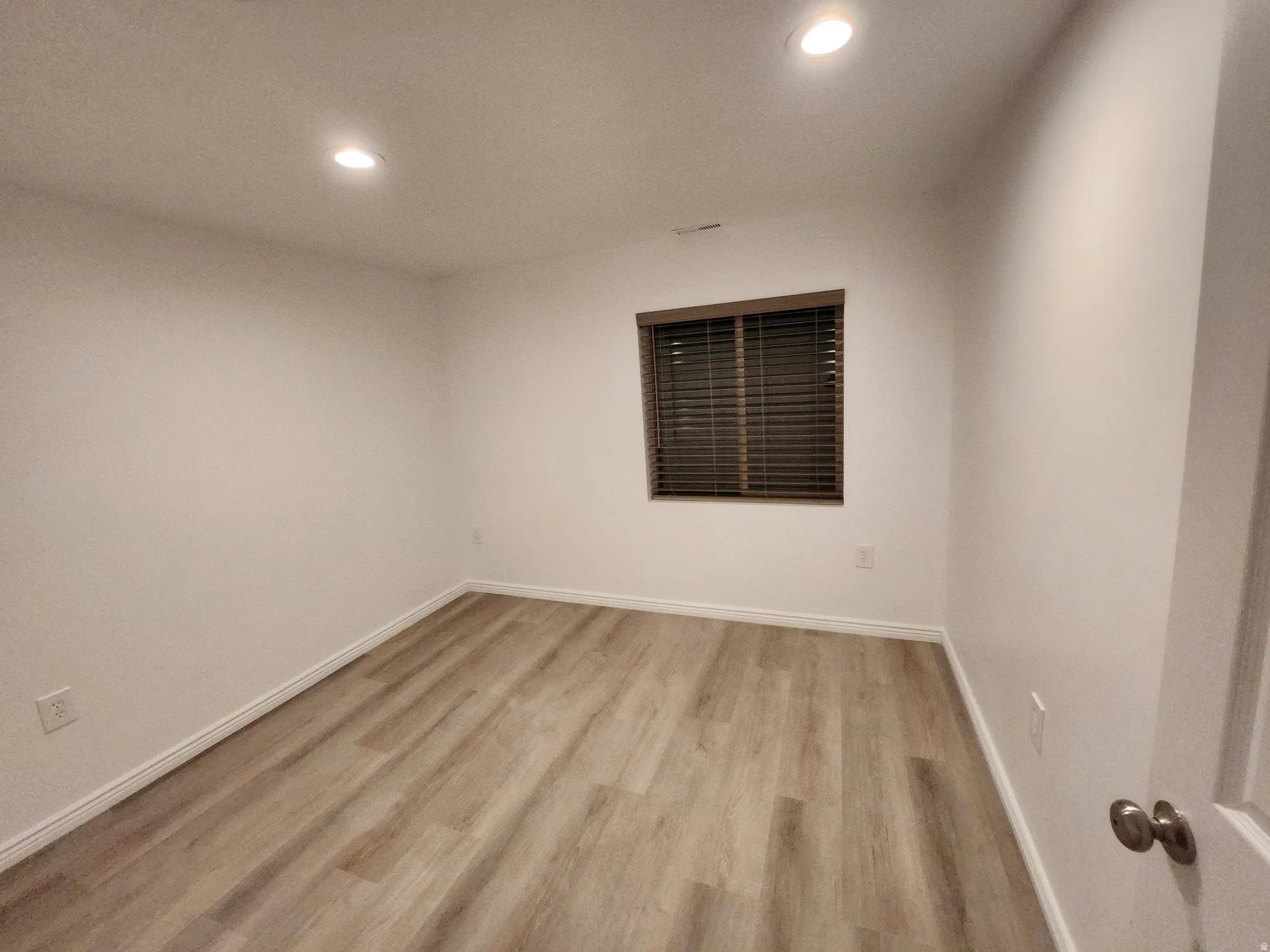 Room featuring recessed lighting, light wood-finish flooring, white baseboards, and a window with dark wood blinds