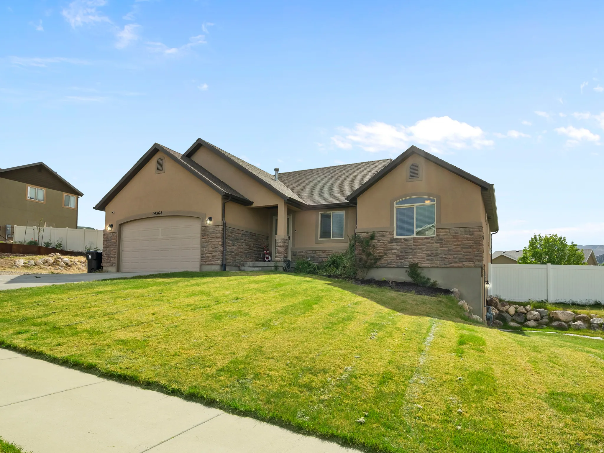 Front exterior with a partial stone facade, attached two-car garage, arched window, and sloped lawn