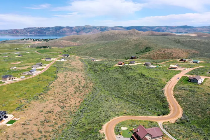 Expansive land featuring a winding dirt road, scattered residential properties, and distant water body