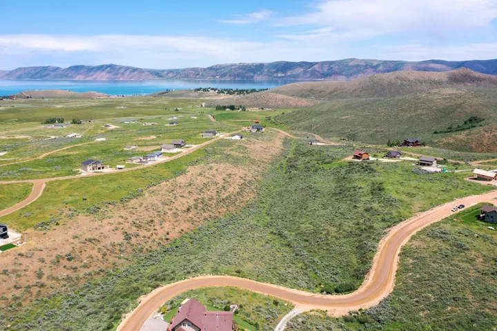 Expansive undeveloped terrain featuring rolling hills, scattered residential structures, and distant water