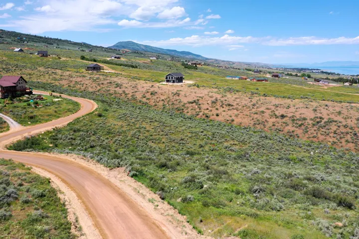 Expansive elevated lot featuring a rugged dirt road, natural vegetation, distant mountains, and a body of water