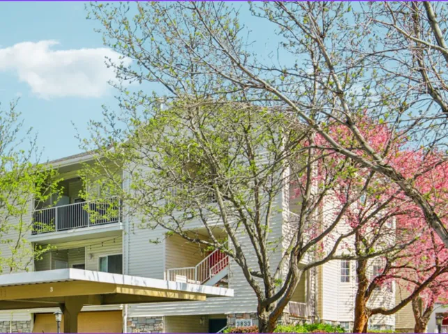 Multi-story building featuring light-colored siding, stone-look foundation, and private balconies with black railings