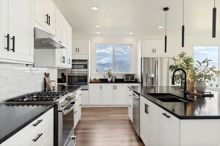 Modern kitchen featuring white shaker cabinetry, dark countertops, stainless steel appliances, a subway tile backsplash, and wood-finish flooring