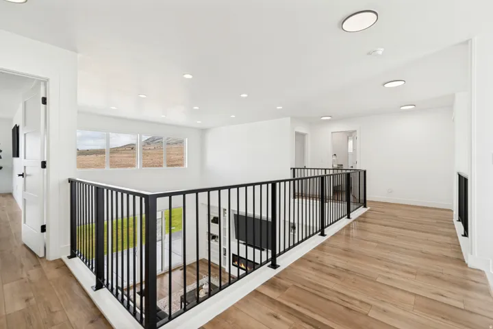 Upper-level landing featuring wood-finish flooring, a contemporary black metal railing, recessed lighting, and multiple windows providing natural light and exterior scenery