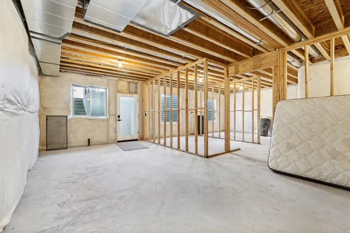 Unfinished basement featuring exposed wood joists, concrete flooring, framed interior walls, visible ductwork, and an exterior door with a window